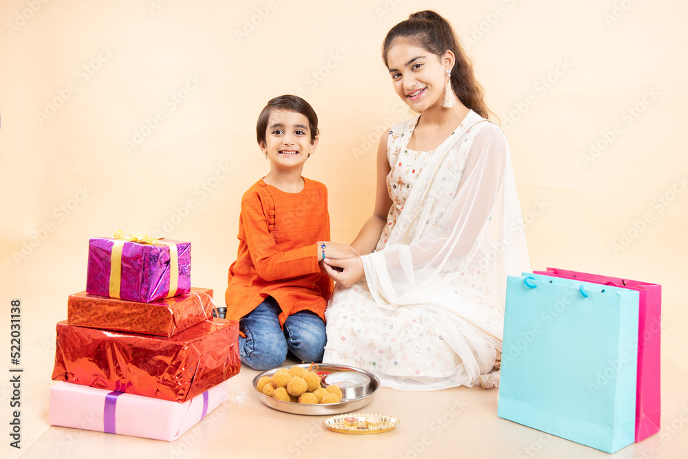 Portrait of happy indian girl tying rakhi on young brother's hand occasion of rakshabandha or bhi dooj isolated on white studio background. both wearing traditional festive cloths. Portrait of happy indian girl tying rakhi on young brother's hand occasion of rakshabandha or bhi dooj isolated on white studio background. both wearing traditional festive cloths.