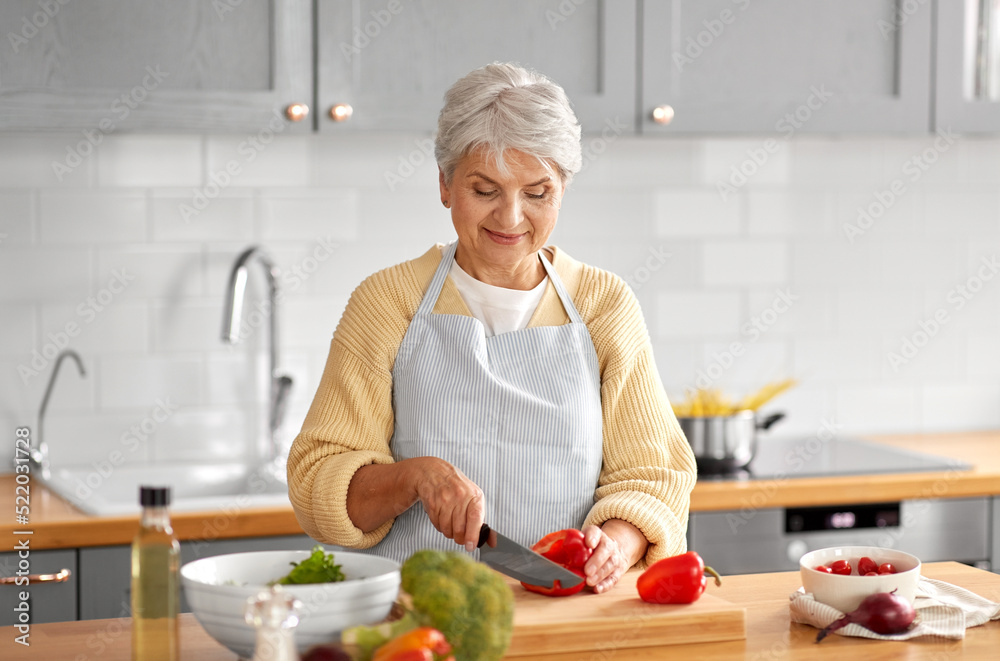 healthy eating, food cooking and culinary concept - happy smiling senior woman with knife chopping red pepper on kitchen at home healthy eating, food cooking and culinary concept - happy smiling senior woman with knife chopping red pepper on kitchen at home