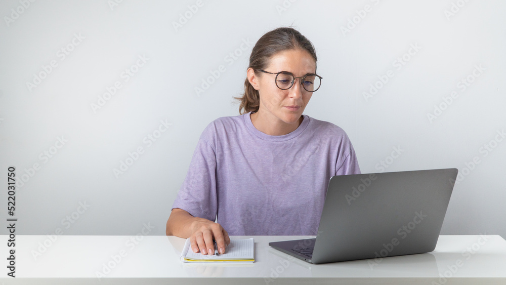 A female student sits at a laptop with a notebook and a pen A female student sits at a laptop with a notebook and a pen