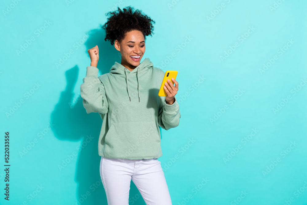 Portrait of delighted funny girl raise fist celebrate success hold telephone isolated on aquamarine color background Portrait of delighted funny girl raise fist celebrate success hold telephone isolated on aquamarine color background