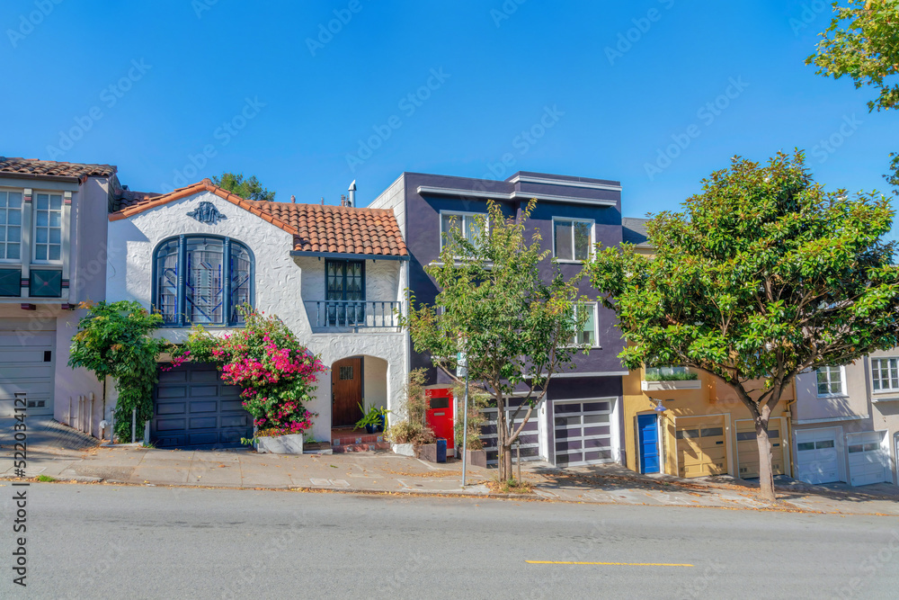 Sloped row of houses in San Francisco, California with trees and plants near the sidewalk