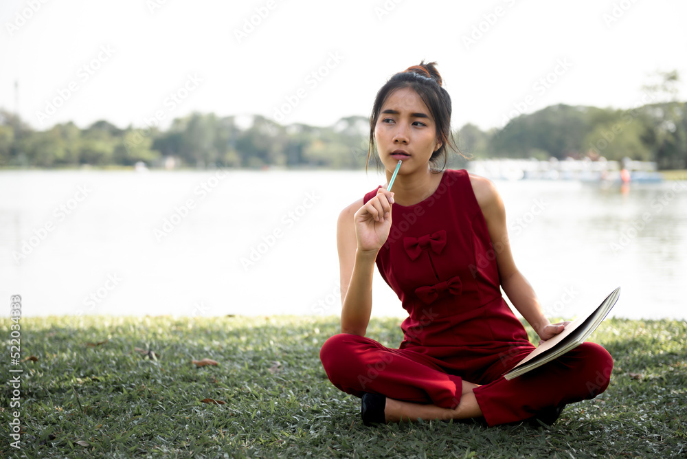 Young Asian woman sitting on green grass reading a book in the park ...