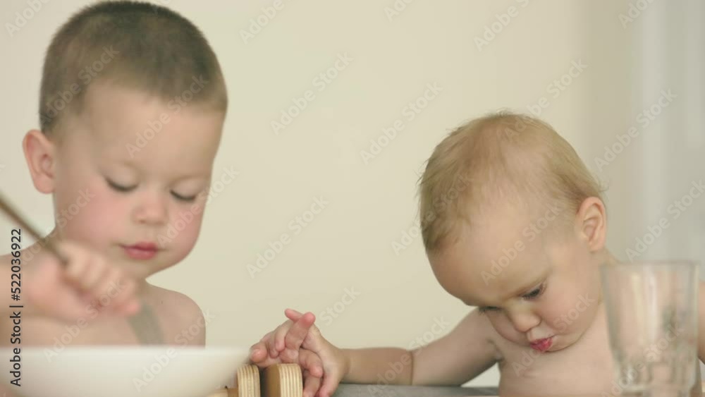 little baby boys feeding pasta each other with fork from plate in kitchen, children eating fusilli macaroni. sibling boy kids having lunch together. naked caucasian brothers care relations. little baby boys feeding pasta each other with fork from plate in kitchen, children eating fusilli macaroni. sibling boy kids having lunch together. naked caucasian brothers care relations.