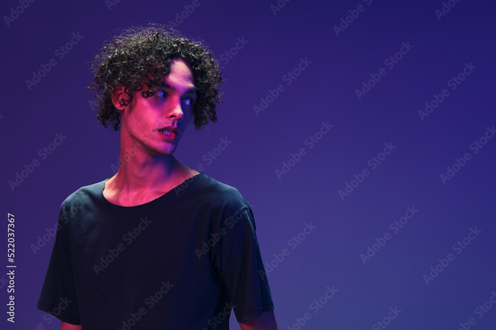 Fashionable handsome curly man in black t-shirt looks aside posing isolated on color pink blue studio background. Cool fashion offer. Virtual Reality New Collection concept. Copy space for ad Fashionable handsome curly man in black t-shirt looks aside posing isolated on color pink blue studio background. Cool fashion offer. Virtual Reality New Collection concept. Copy space for ad