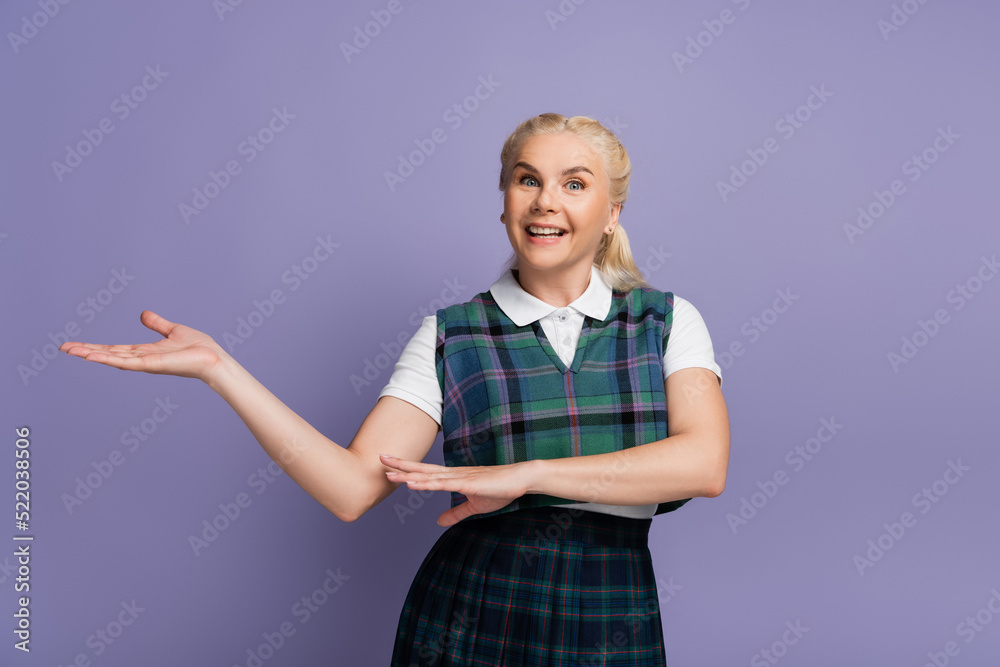 Cheerful student in uniform pointing with hand isolated on purple Cheerful student in uniform pointing with hand isolated on purple