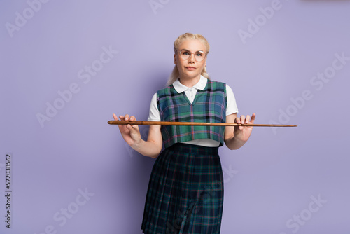 Student in uniform holding pointer and looking at camera on purple background