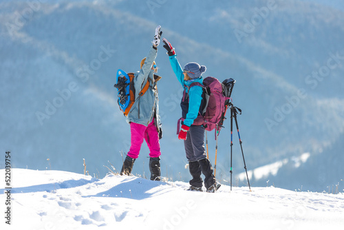 two women climbed to the top of the mountain during a winter hike, girl gives high five to friend