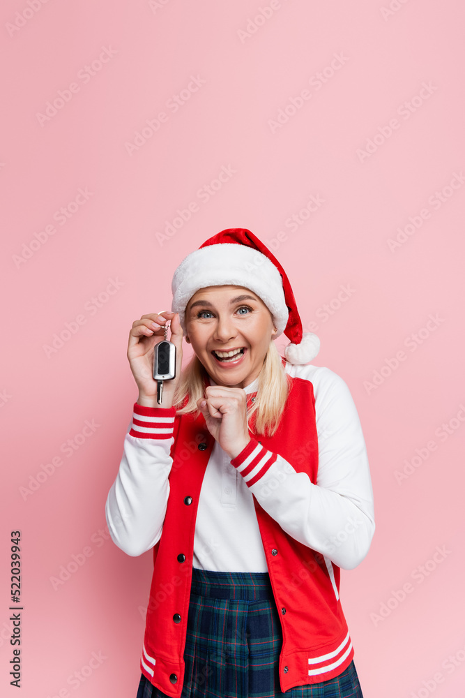 Excited woman in santa hat holding car key and showing yes gesture isolated on pink Excited woman in santa hat holding car key and showing yes gesture isolated on pink