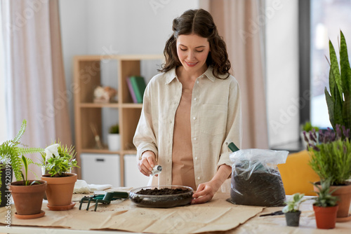 people, gardening and housework concept - happy woman pouring seeds to soil in glass vase and planting flowers at home