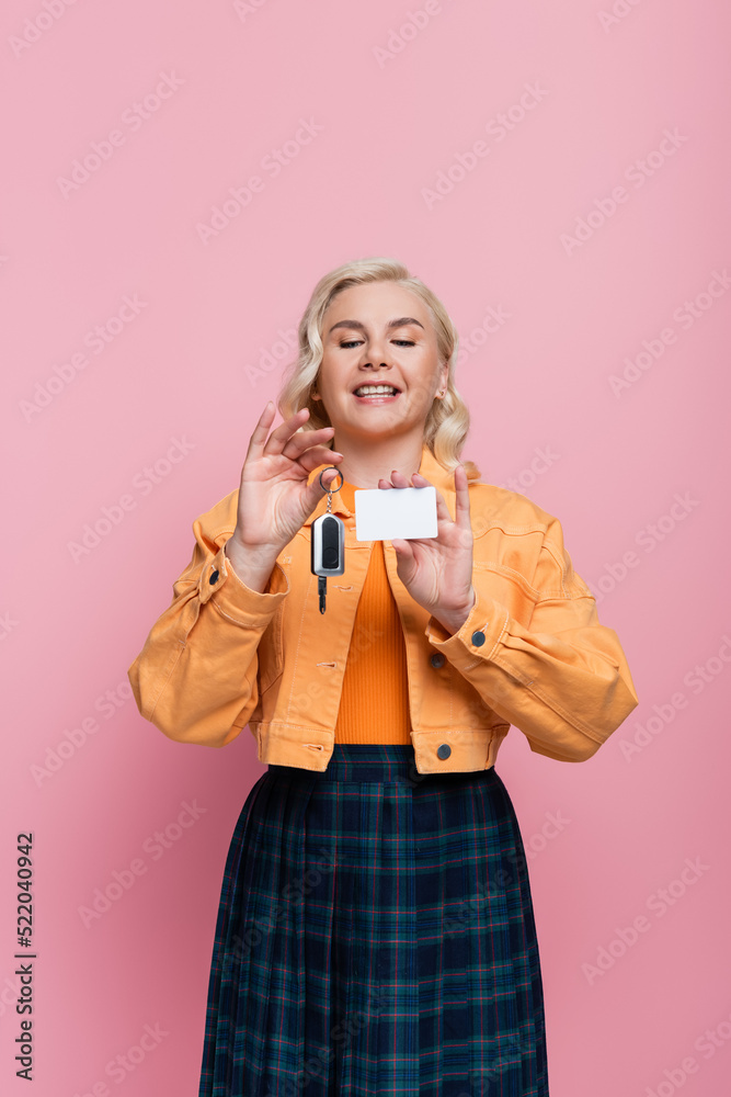 Happy driver holding car key and empty driving license isolated on pink