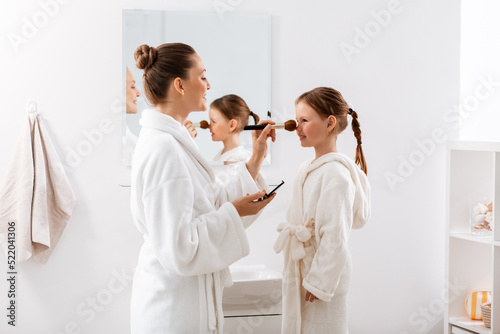 beauty, family and people concept - happy smiling mother and little daughter with brush and powder applying make up in bathroom