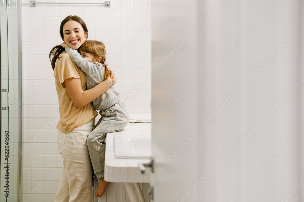 White woman smiling while hugging her daughter in bathroom White woman smiling while hugging her daughter in bathroom