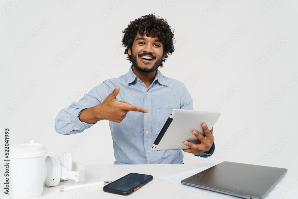 Happy smiling indian man sitting at office table with tablet Happy smiling indian man sitting at office table with tablet
