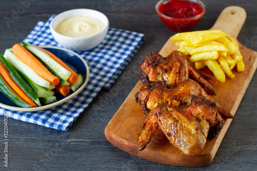 Spicy chicken wings and french fries with sauces. Food lunch or dinner, typical fast food. on a wooden background.