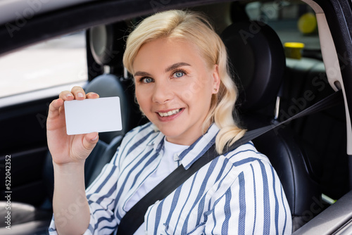 Cheerful woman holding driver license in auto