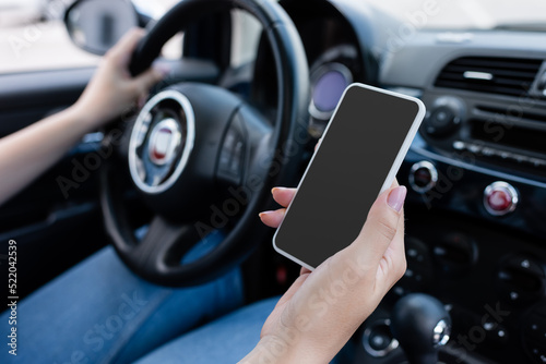 Cropped view of blurred woman holding smartphone with blank screen in blurred car