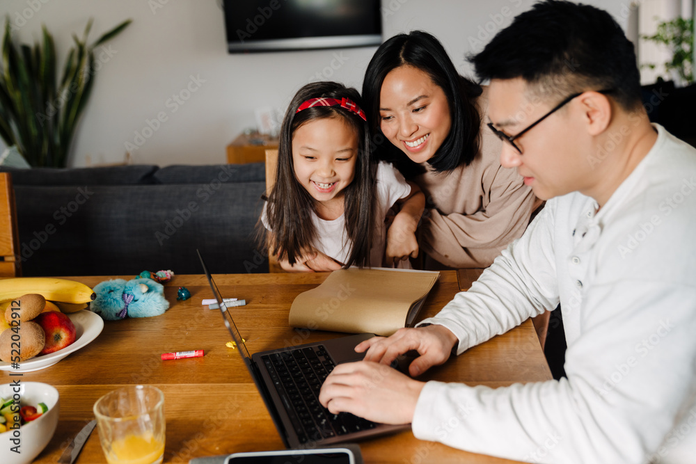 Happy asian family with daughter using laptop over table at home Happy asian family with daughter using laptop over table at home