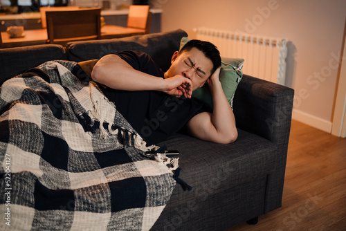Canvas Print Adult asian tired man lying on the sofa and yawning