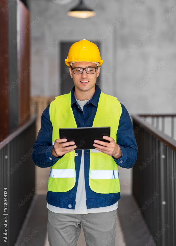 architecture, construction business and building concept - happy smiling male architect in helmet and safety west with tablet pc computer at office architecture, construction business and building concept - happy smiling male architect in helmet and safety west with tablet pc computer at office