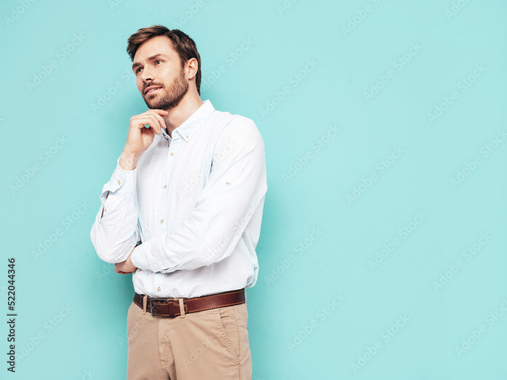 Portrait of handsome smiling model. Sexy stylish man dressed in shirt and trousers. Fashion hipster male posing near blue wall in studio. Thoughtful Portrait of handsome smiling model. Sexy stylish man dressed in shirt and trousers. Fashion hipster male posing near blue wall in studio. Thoughtful