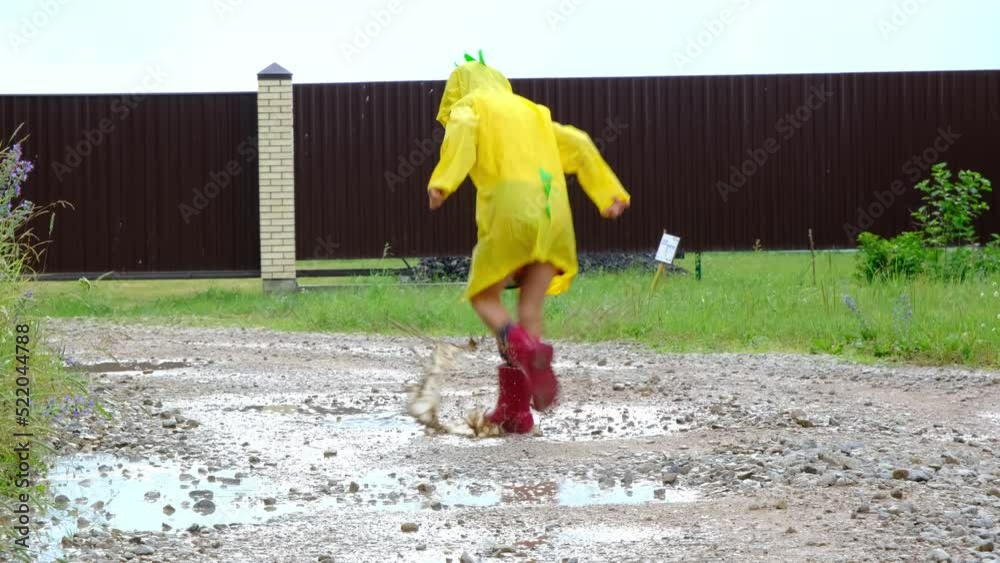 A girl in red rubber boots and a yellow raincoat runs through puddles ...