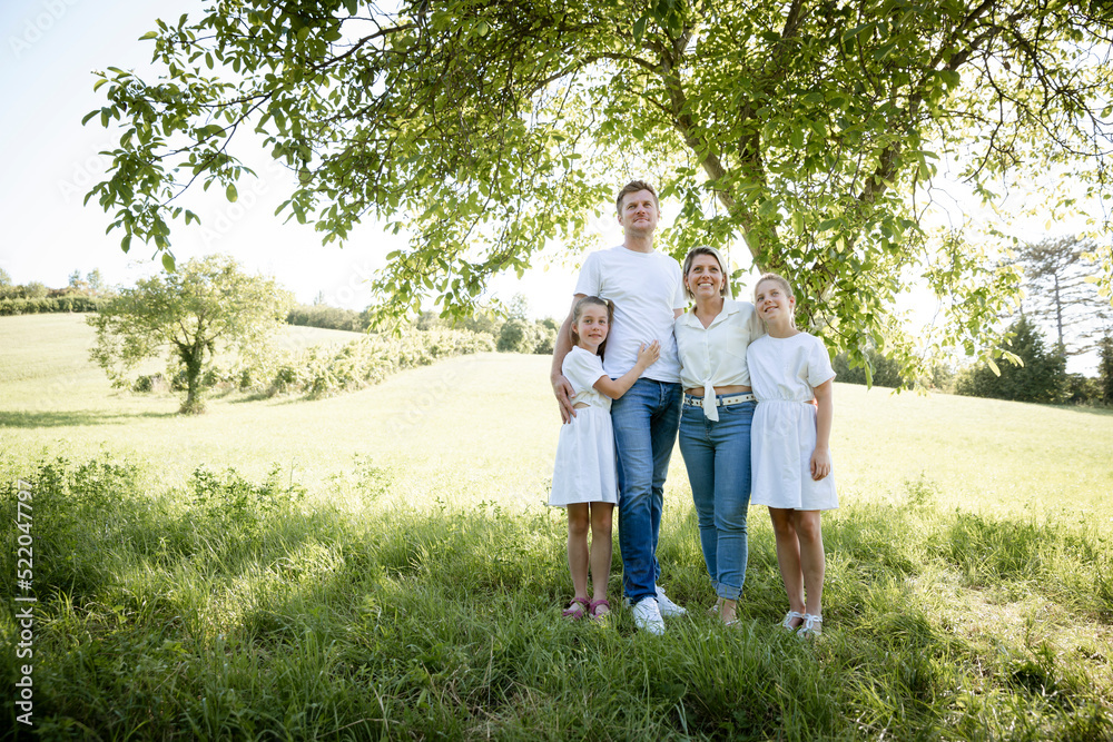 beautiful family with two girls is standing in meadow near walnut tree and has light outfit on and jeans and is happy beautiful family with two girls is standing in meadow near walnut tree and has light outfit on and jeans and is happy