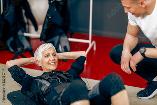 Senior Woman Doing Crunches Exercise During EMS Workout With Coach In The Gym