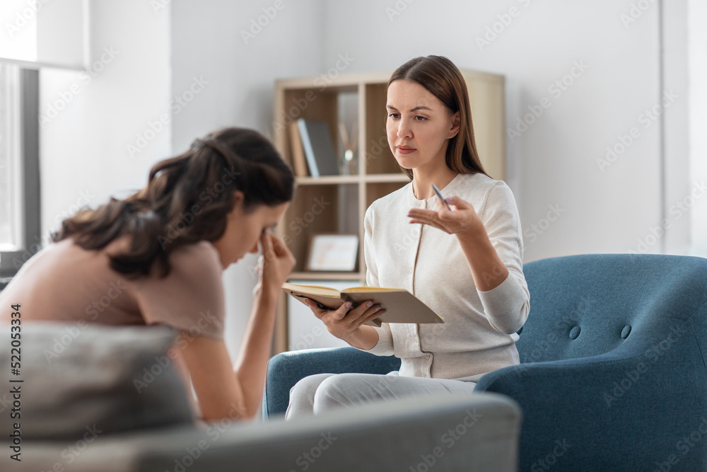 psychology, mental health and people concept - psychologist with notebook talking to stressed woman patient at psychotherapy session - obrazy, fototapety, plakaty 