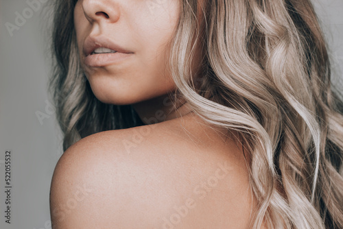 Cropped shot of a young caucasian beautiful woman with blond wavy hair isolated on a gray background. Result of coloring, highlighting, perming