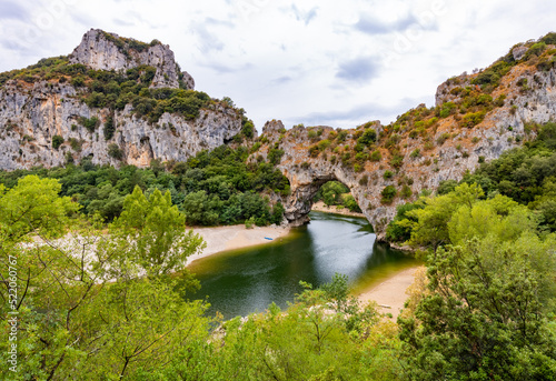 “Pont d’Arc“ panorama in Vallon South France. Large natural bridge or rock arch spanning over Ardèche river in Provence. Major tourist attraction and sight in calm morning atmosphere on a cloudy day. photo