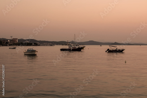 View of small, wooden fishing boats, Aegean sea and landscape at sunset captured in Ayvalik area of Turkey in summer. Beautiful scene.