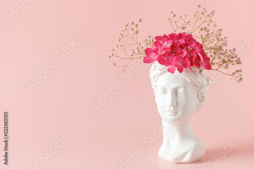 Creative art concept plaster head ancient sculpture with hair fresh flowers gypsophila and hydrangea on pink background. Copy space