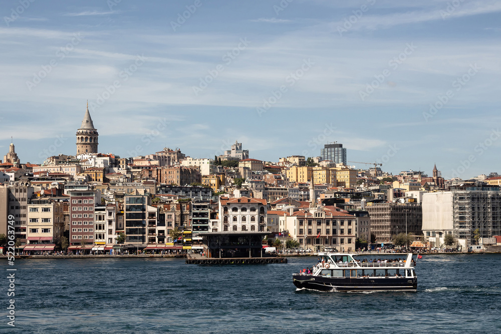 View of a tour boat on Golden Horn part of Bosphorus in Istanbul. Galata tower and Beyoglu district are in the view. It is a sunny summer day.