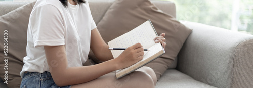 Asian woman writes notebook or a diary on her bedroom couch at home during the holidays, New work lifestyle, Relaxation, Happy time, Living at home, Sit comfortably on vacation, Comfortable corner.