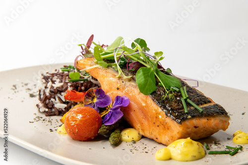 Salmon steak with skin on garnished with microgreens on a plate against a white background