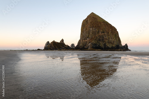 Dawn at monolith Haystack Rock at Cannon Beach Oregon with a reflection in wet sand with ripples in the early morning