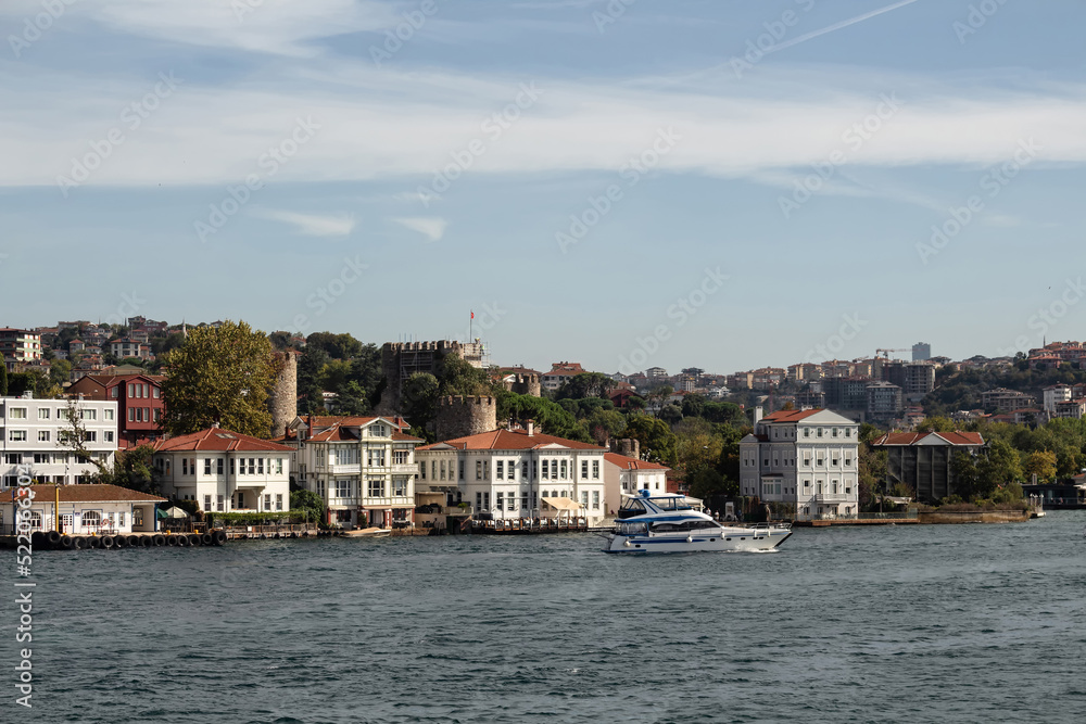 View of historical, traditional mansions by Bosphorus in Anadolu Hisari area of Asian side of Istanbul. Luxury yacht passes. It is a sunny summer day. Beautiful travel scene.