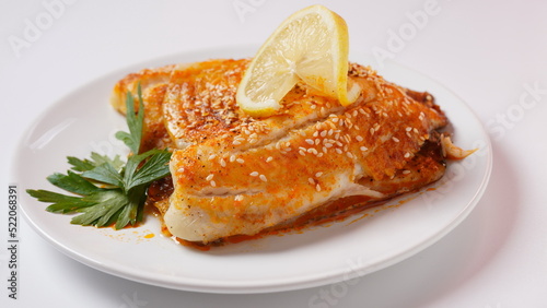 Fresh backed tilapia fillet on white plate with lemon and herbs