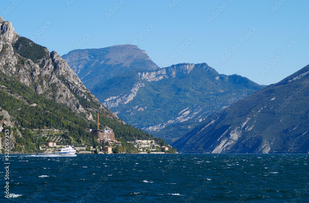 a beautiful old harbor with sailing boats in the mediterranean Italian town of Limone sul Garda on turquoise lake Garda with mountains in the background (Italy, Lombardy)
