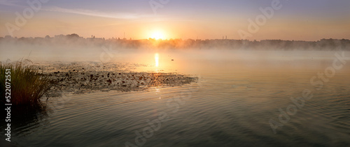 The sun rising over the lake, morning sunrise panorama with fog on the water