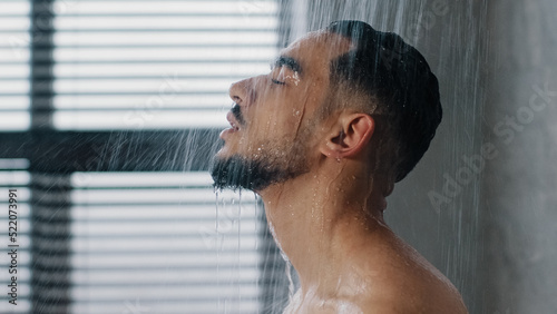 Slika na platnu Side view closse up Arab relaxed man bearded guy naked male washes head hair face and beard in bathroom showering in at home in hotel after workout close up