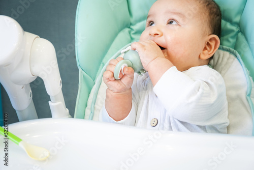 A happy and contented baby eats banana puree from a nipple. Introduction of complementary foods, healthy baby food, feeding the baby at the table