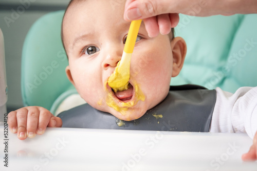 Fotografi Mom feeds the baby with a spoon of vegetable puree at the children's feeding table