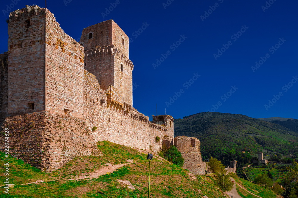 View of Rocca Maggiore (Great Fortress) ancient ruins, at the top of the city of Assisi, with medieval walls and Mount Subasio