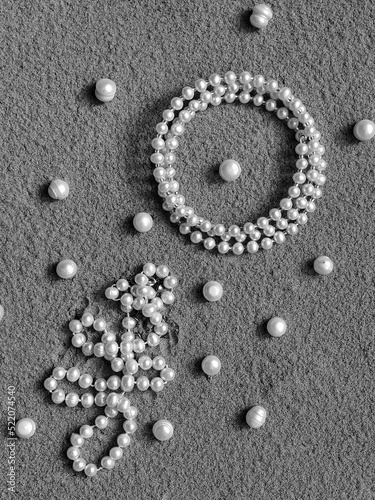 Pearl jewelry and pearl beads on the sand. A creative wedding concept with white necklace and a pearl bracelet. Summer background with pearls on the sand.