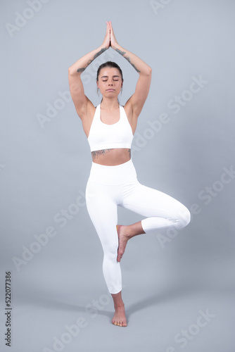 Young sporty woman in sportswear, practicing yoga, beautiful girl doing exercise, working out on gray studio background.
