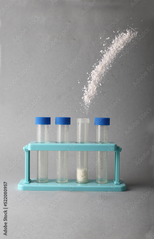 white powder pouring into test tube against gray background white powder pouring into test tube against gray background