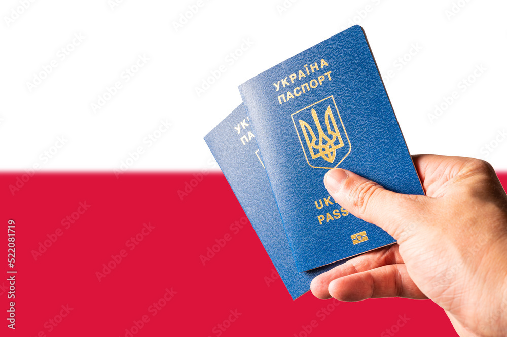 Two Ukrainian biometric passports in a man's hand against the background of the national flag of Poland. Travel, tourism, refugees, war in Ukraine, business, asylum in Europe. Two Ukrainian biometric passports in a man's hand against the background of the national flag of Poland. Travel, tourism, refugees, war in Ukraine, business, asylum in Europe.