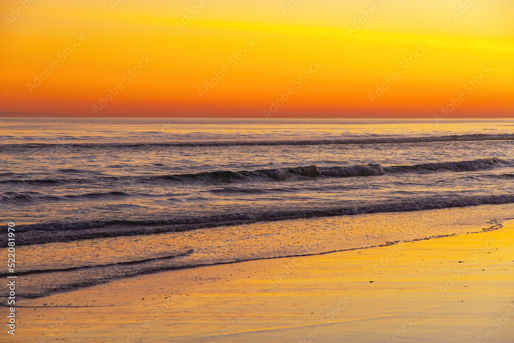 Waves at sunset on the beach with reflections of the orange sky in the sea water