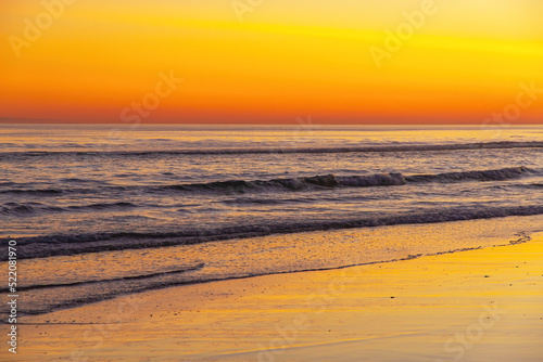 Waves at sunset on the beach with reflections of the orange sky in the sea water